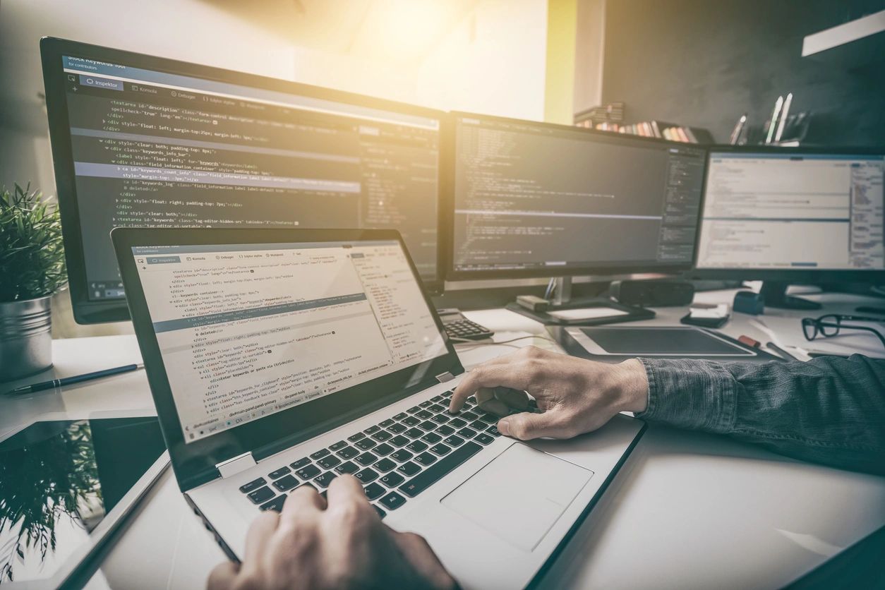 A person is using a laptop in front of multiple monitors.